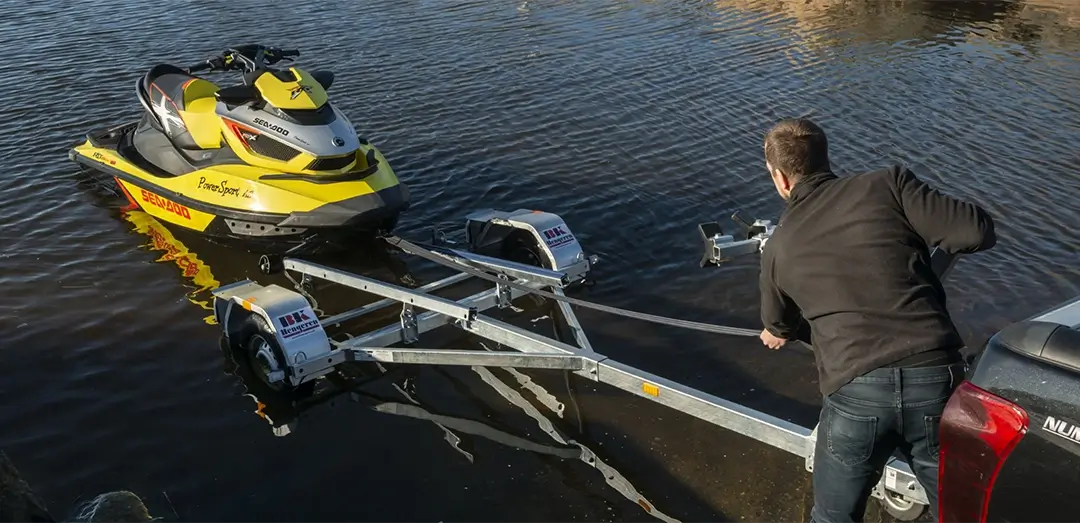 En gul vannscooter i sjøen er på vei opp en vannscooterhenger.
